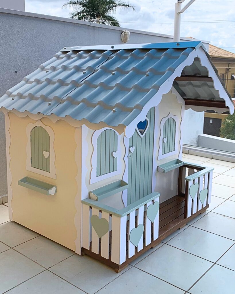 Casinha infantil de madeira pintada em cores suaves com detalhes em forma de coração, ideal para brincadeiras ao ar livre 