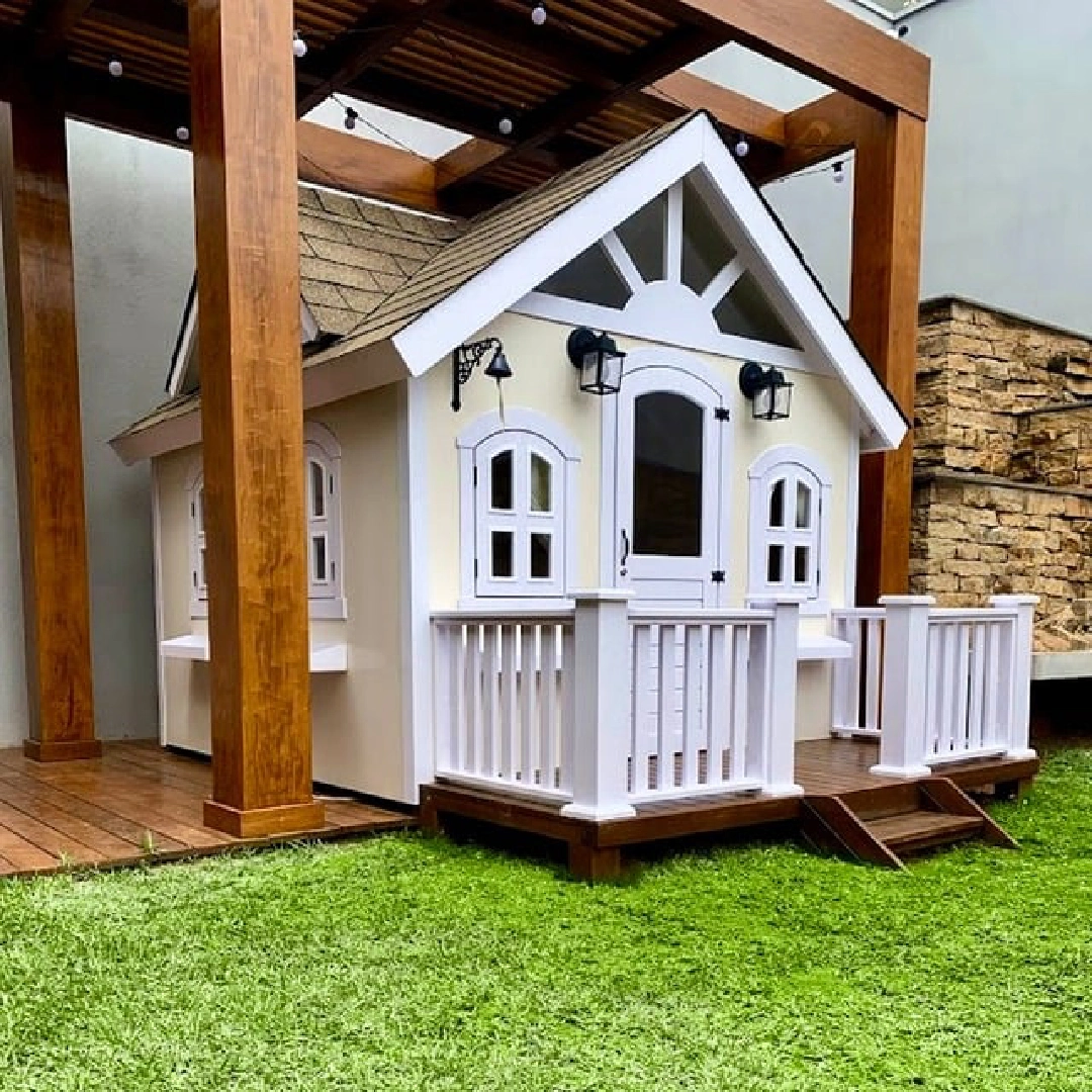 Casinha-castelo grande de madeira cinza com escorregador e bandeiras.