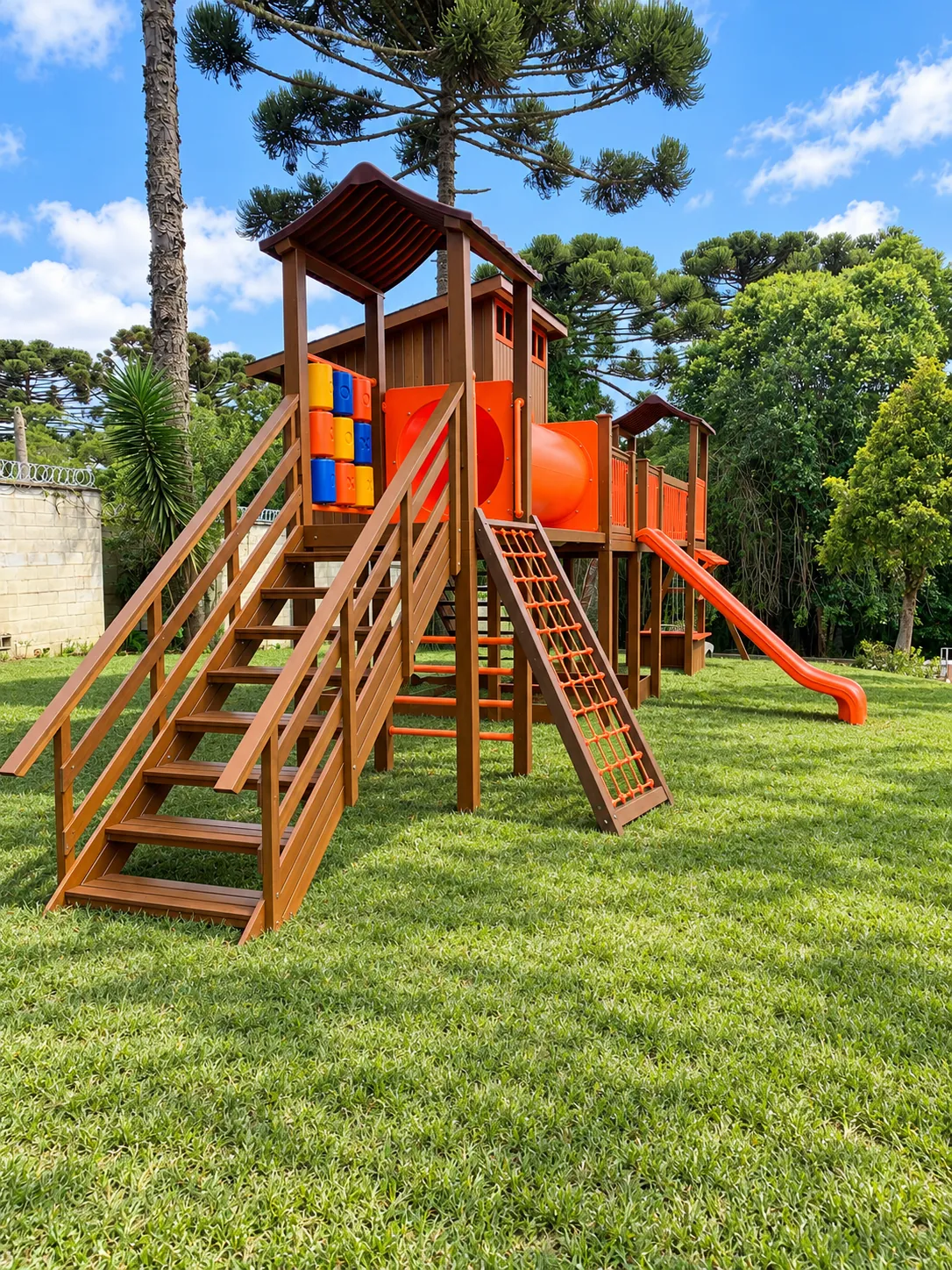 Playground de madeira com duas torres, túnel laranja, escada com corrimão e escalada de cordas